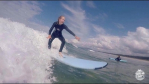 Nuori nainen surffilaudalla aallonharjalla.