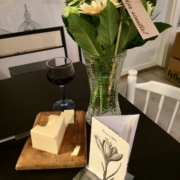 Kukkia, juusto, viiniä ja tervetulokortti pöydällä.