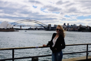 Nuori nainen Sydneyn oopperatalon edustalla hiukset tuulessa hulmuten.