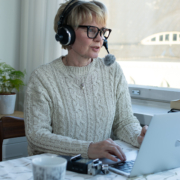 Tuija nauhoittamassa podcastjaksoa tietokoneen ääressä kuulokkeet korvilla.