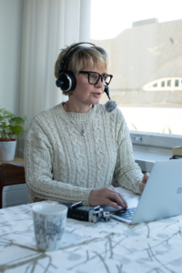 Podcast-päivänä Tuija nauhoittaa uutta jaksoa tietokoneen ääressä kuulokkeet korvilla.