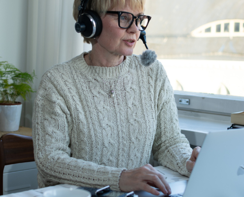 Tuija nauhoittamassa podcastjaksoa tietokoneen ääressä kuulokkeet korvilla.