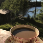 Kahvikupponen pienen punaisen tuvan pihalla järven rannalla.