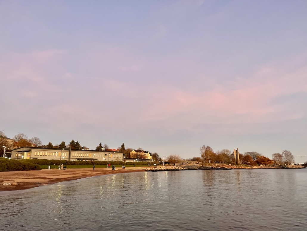 Ihmisiä istuskelemassa rannalla horisonttia ihastelemassa.