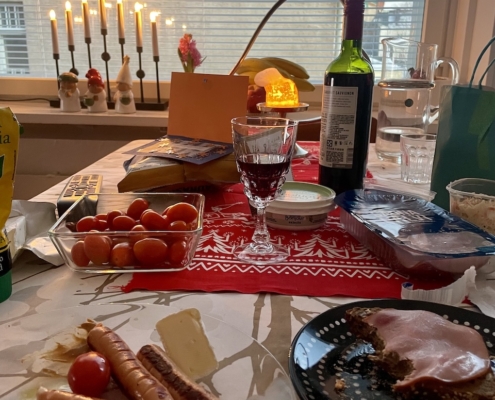 Nakkeja, coleslawsalaattia, brietä, hedelmäleipää ja viiniä lohturuokana pöydässä.