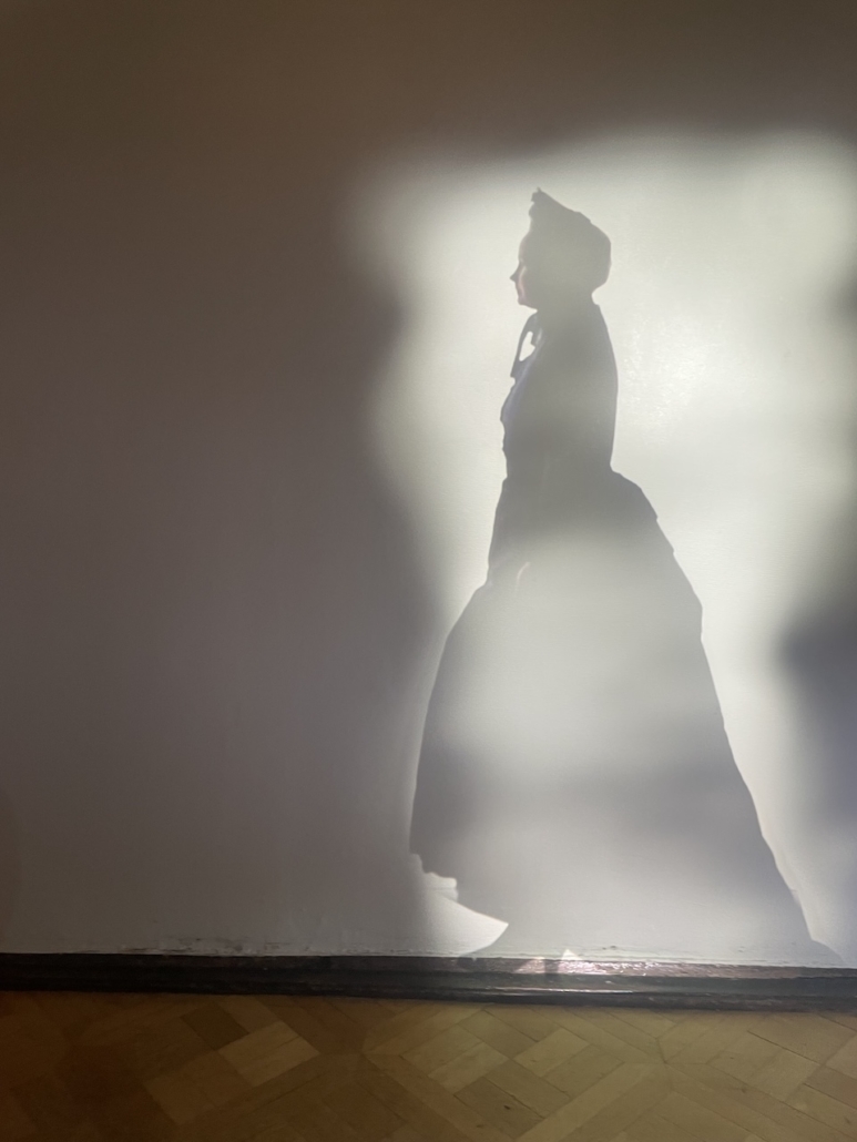 Naisen varjo seinälle heijastuvassa valossa.