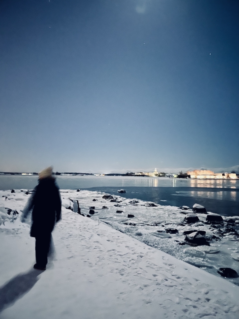 Ihmisen hahmo meren horisontissa näkyviä valoja vasten.