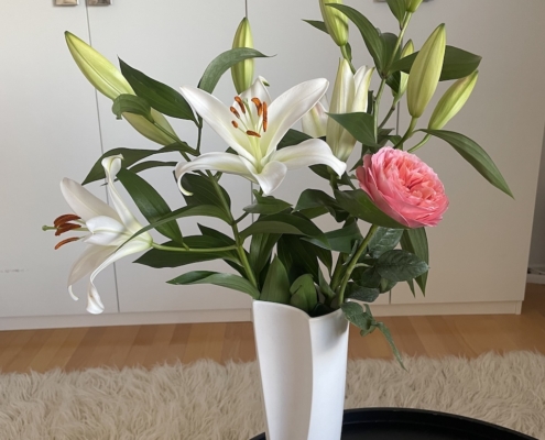 Äitienpäivälahjaksi saadut liljat ja ruusu valkoisessa maljakossa.
