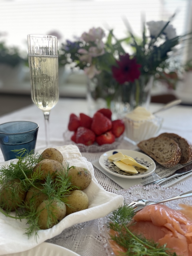 Ruokapöytä, jossa on graavilohta, uusia perunoita sekä mansikoita ja kermavaahtoa kauniisti katettuna.