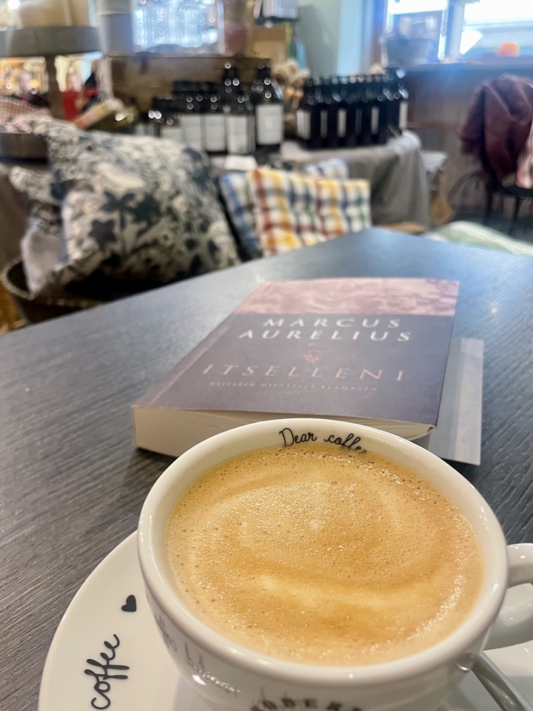 Cappuccino-kuppi ja kirja Itselleni kahvilan pöydässä.