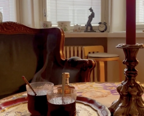 Kaksi lasia jouluglögiä ja palava kynttilä.