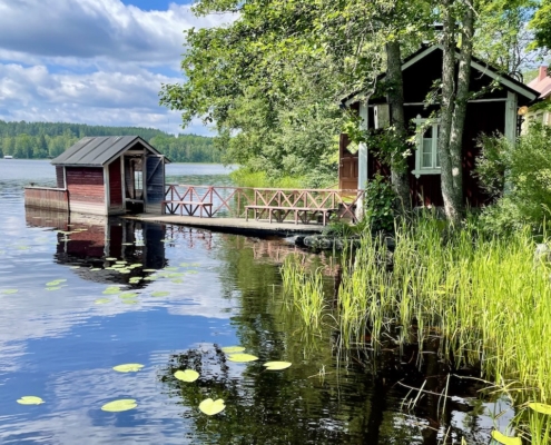 Punainen tupa, laituri ja järvikaislikko.