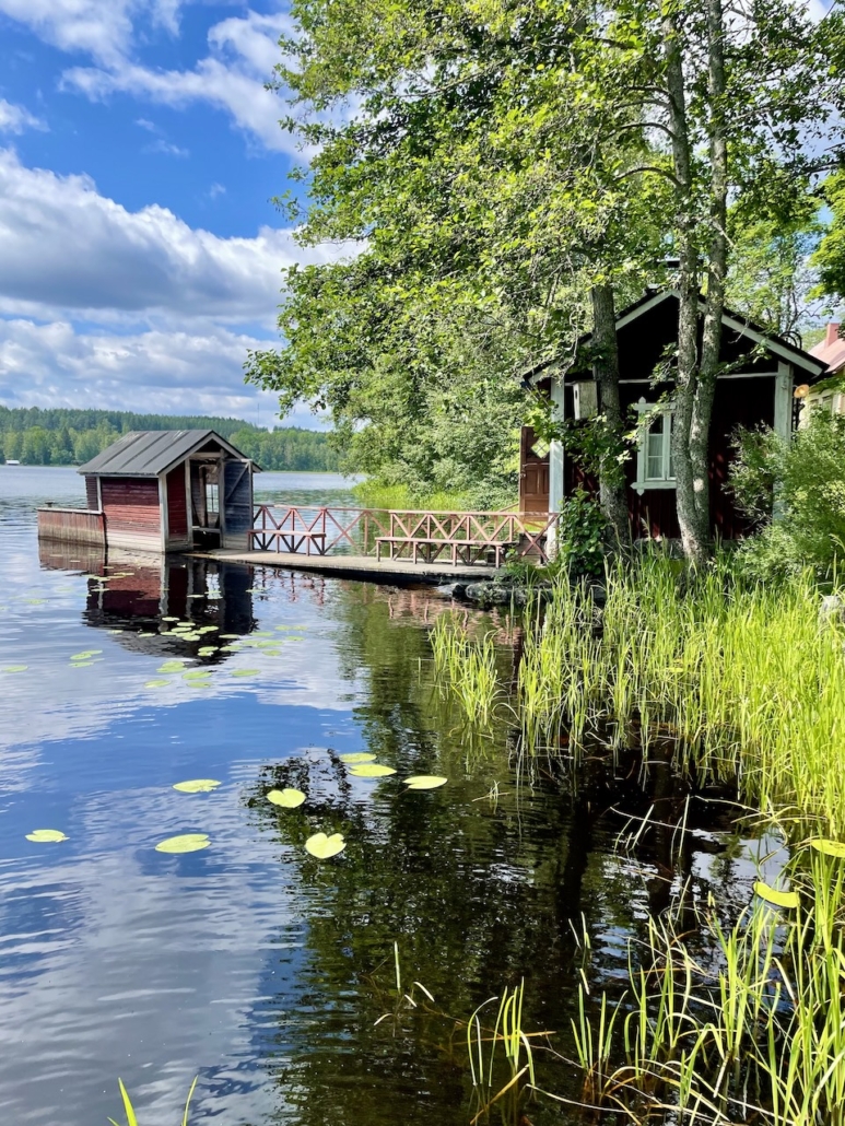 Punainen tupa, laituri ja järvikaislikko.