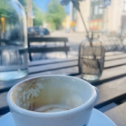 Puoliksi juotu cappuccinokuppi kesäisen terassin pöydällä.