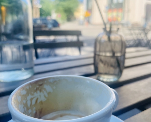 Puoliksi juotu cappuccinokuppi kesäisen terassin pöydällä.