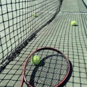 Tennisverkko, kolme tennispalloa ja punainen tennismaila.