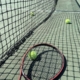 Tennisverkko, kolme tennispalloa ja punainen tennismaila.