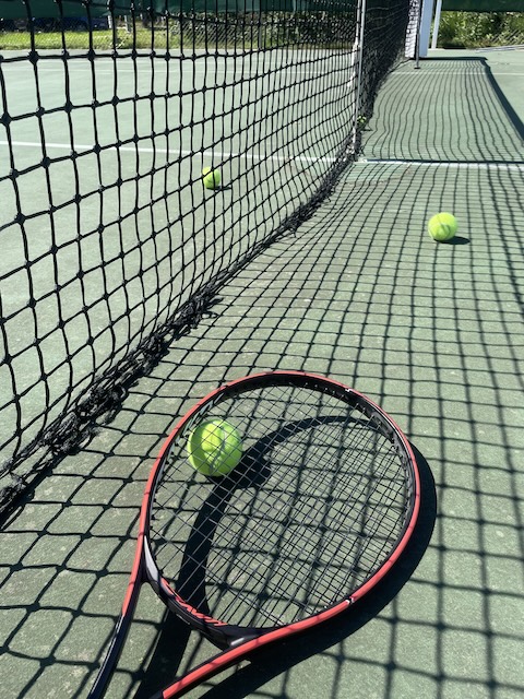 Tennisverkko, kolme tennispalloa ja punainen tennismaila.