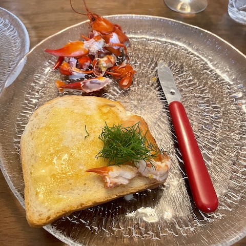 Paahtoleipä, tilliä, rapuveitsi ja rapuja lasilautasella.