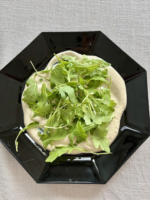 Rucola-tahinipeti Tahinikastiketta ja rucolaa mustalla lautasella.