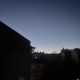 Aamunäkymä ikkunasta, kun on vielä pimeää ja näkyy vain talojen mustat ääriviivat aamutaivasta vasten.